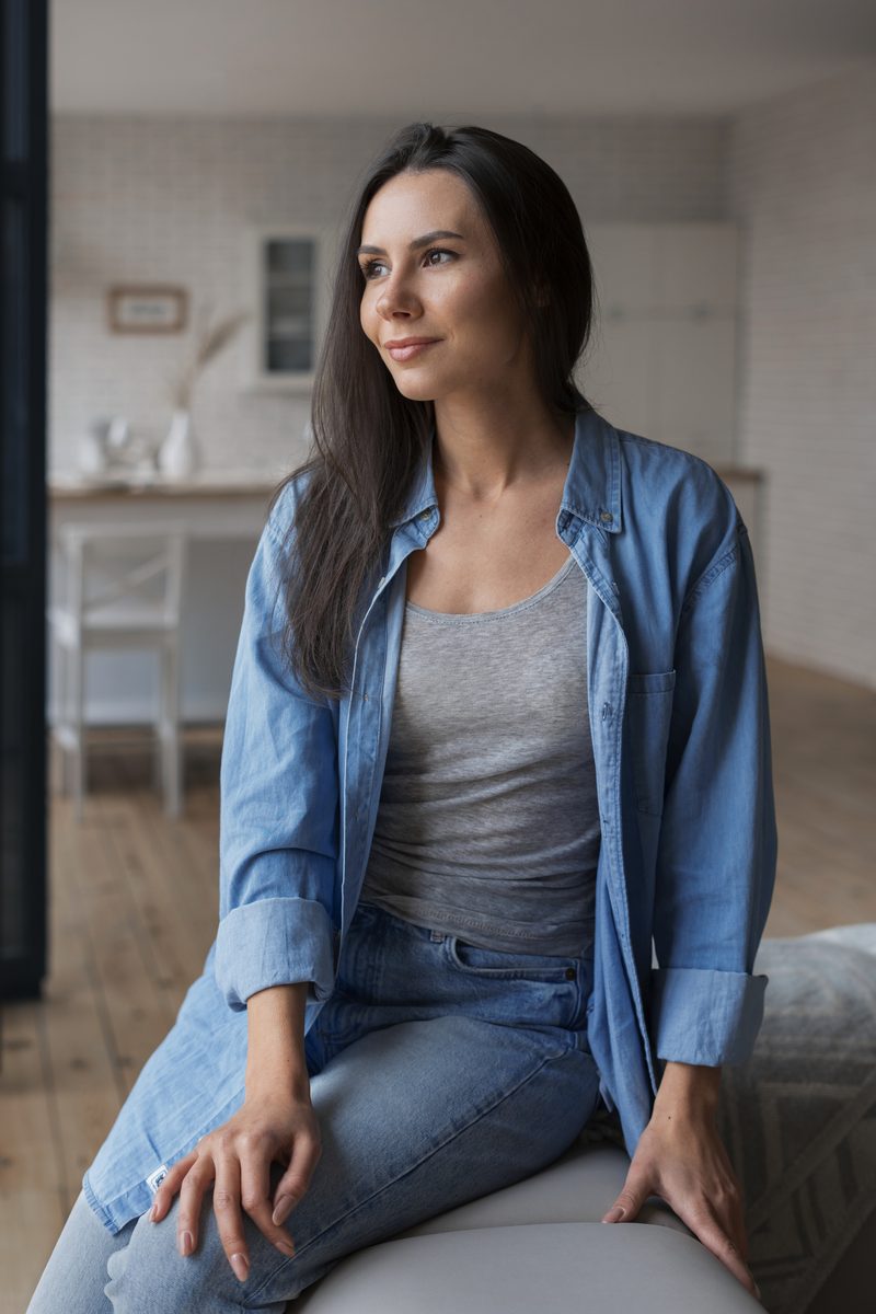 A woman in a denim shirt sitting calmly at home, looking to the side