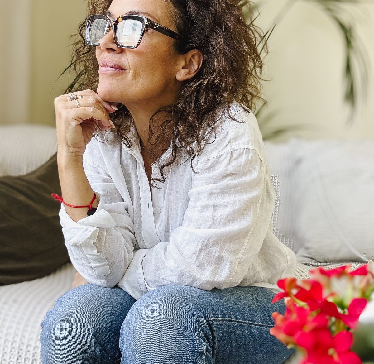 A woman in a white shirt sitting on a sofa, looking away thoughtfully