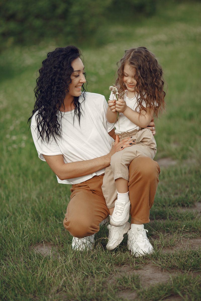 A mother holding her young daughter in a sunlit field