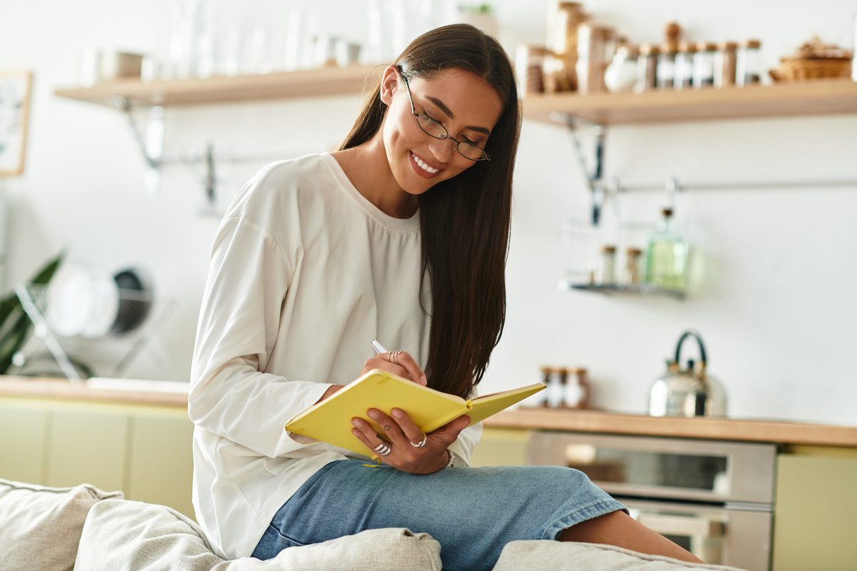 A woman writing in a notebook at home on a bright morning